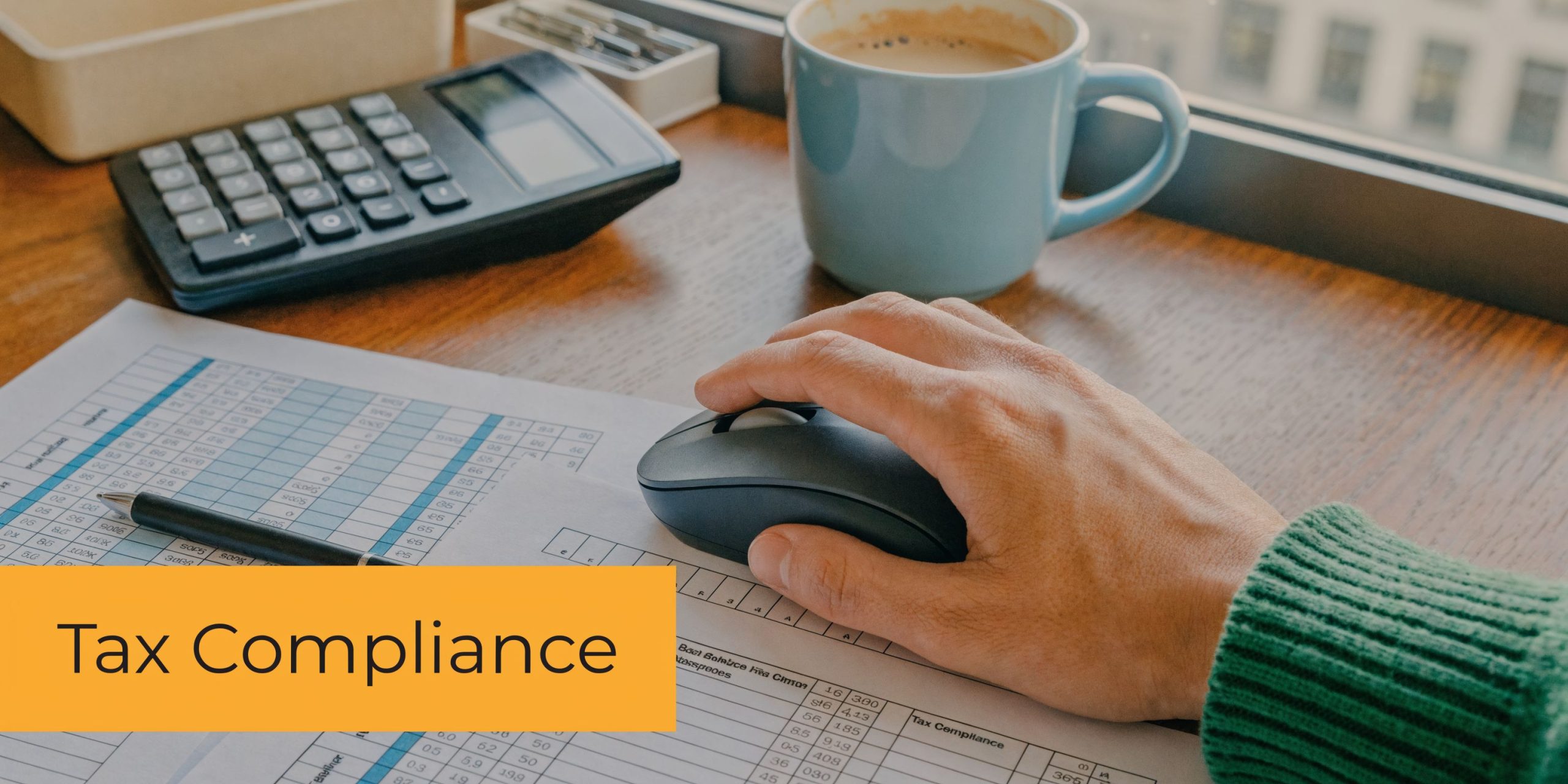 A person uses a computer mouse on a desk with financial documents, a calculator, and coffee.